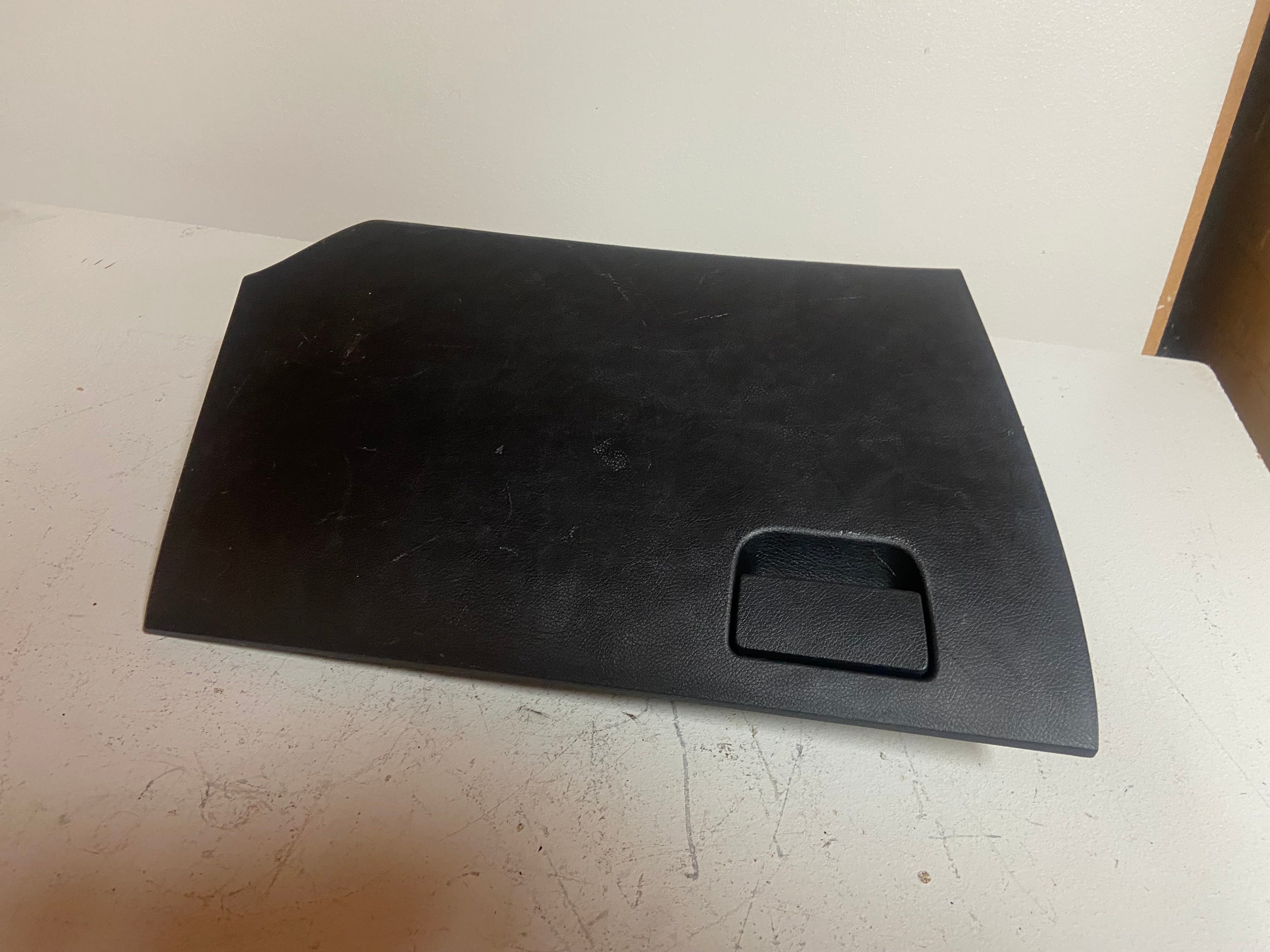 Black glove box lid panel with recessed square handle, flat view