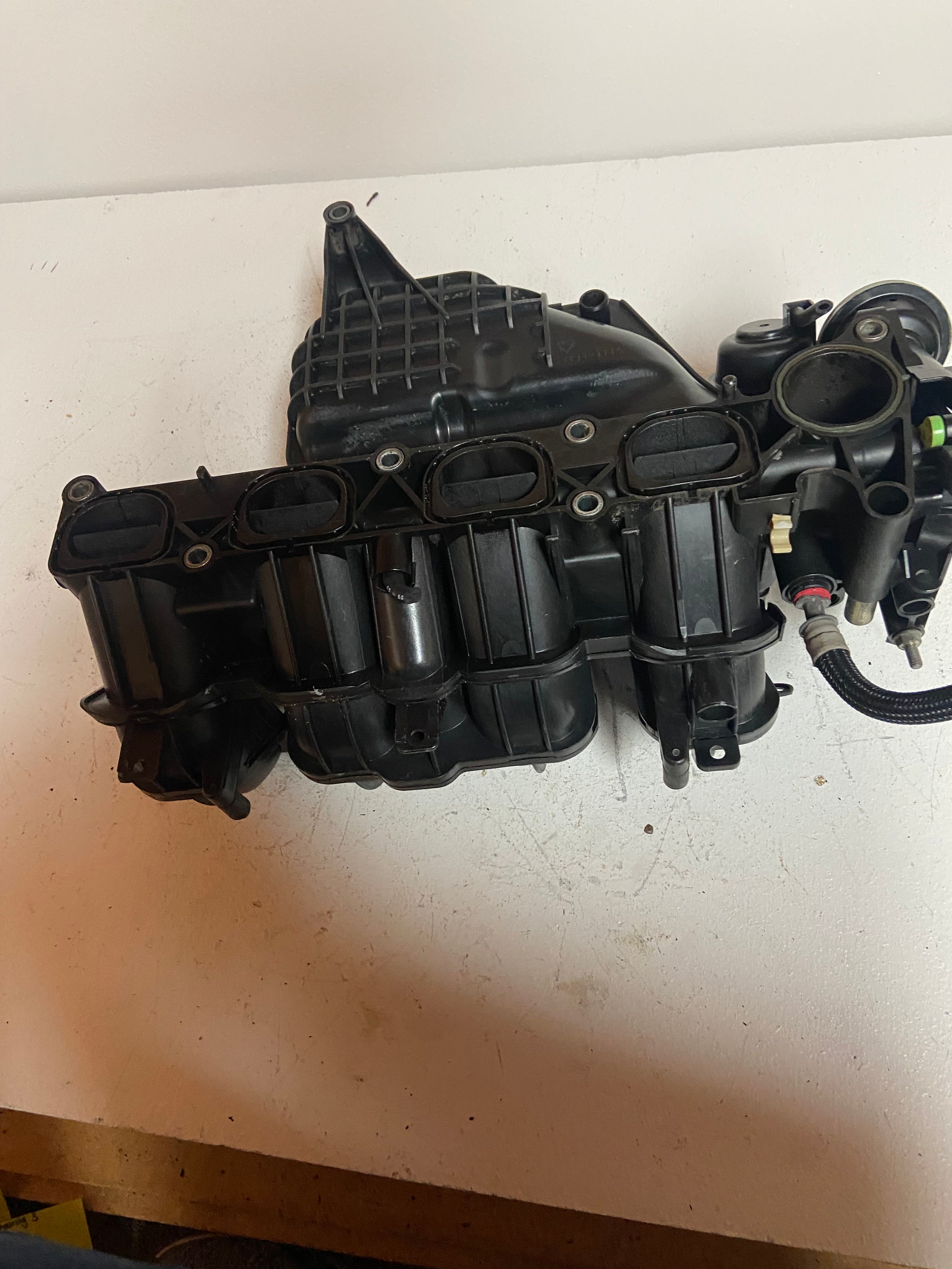 Engine air intake manifold with ribbed plastic housing, sensor port, attached hose