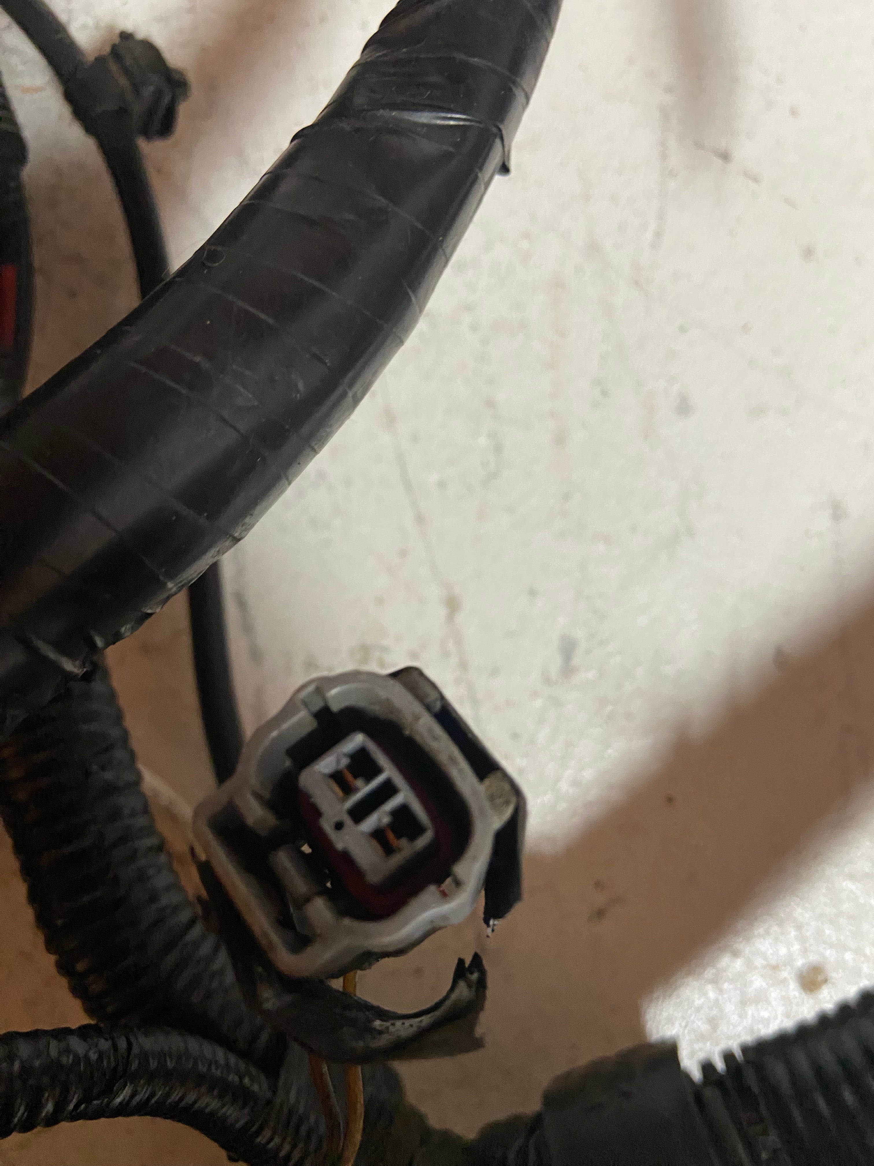 Wiring harness connector plug with locking tab and attached black corrugated cable loom.