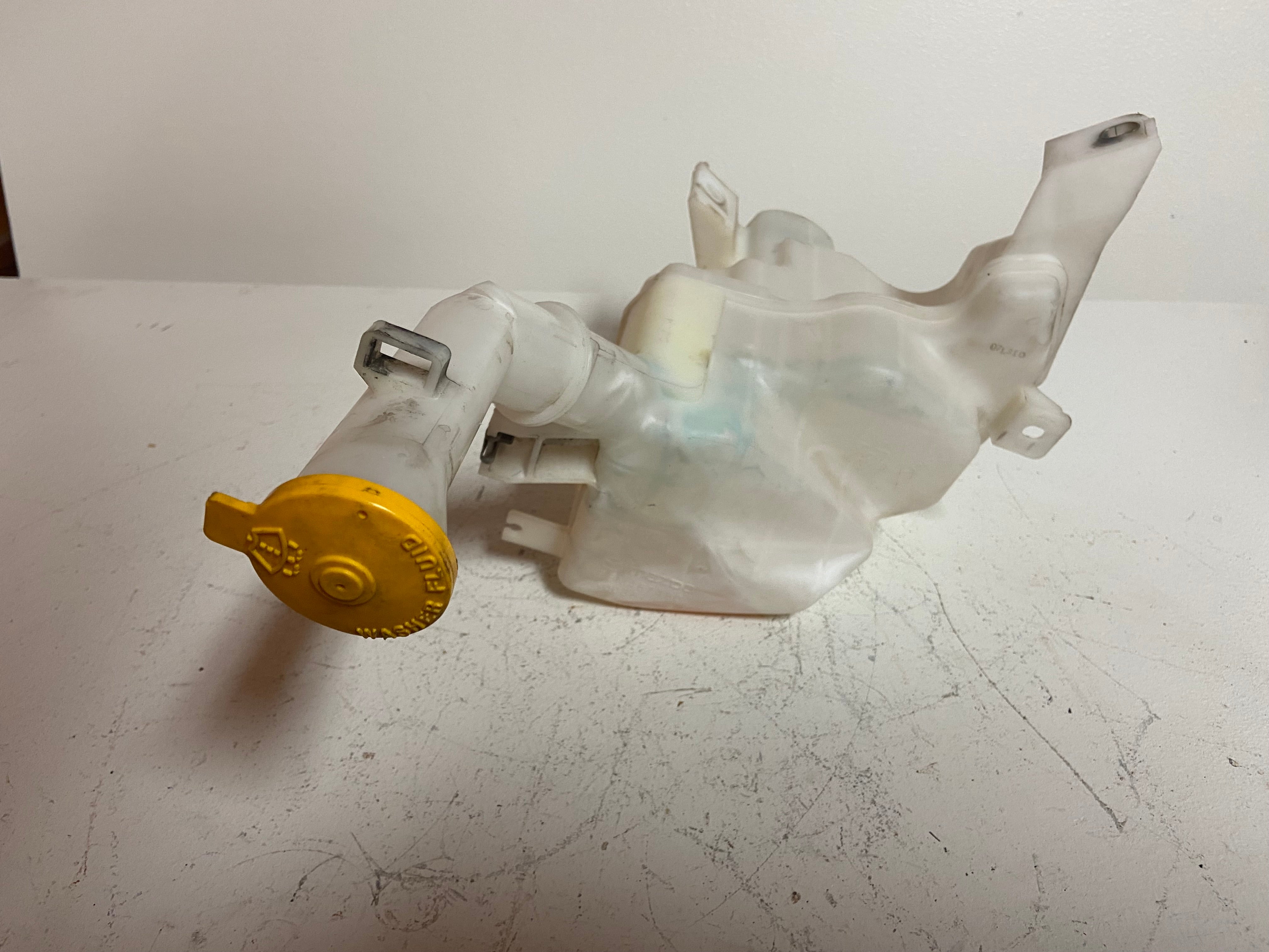 Washer fluid reservoir tank assembly with clear plastic body and yellow cap