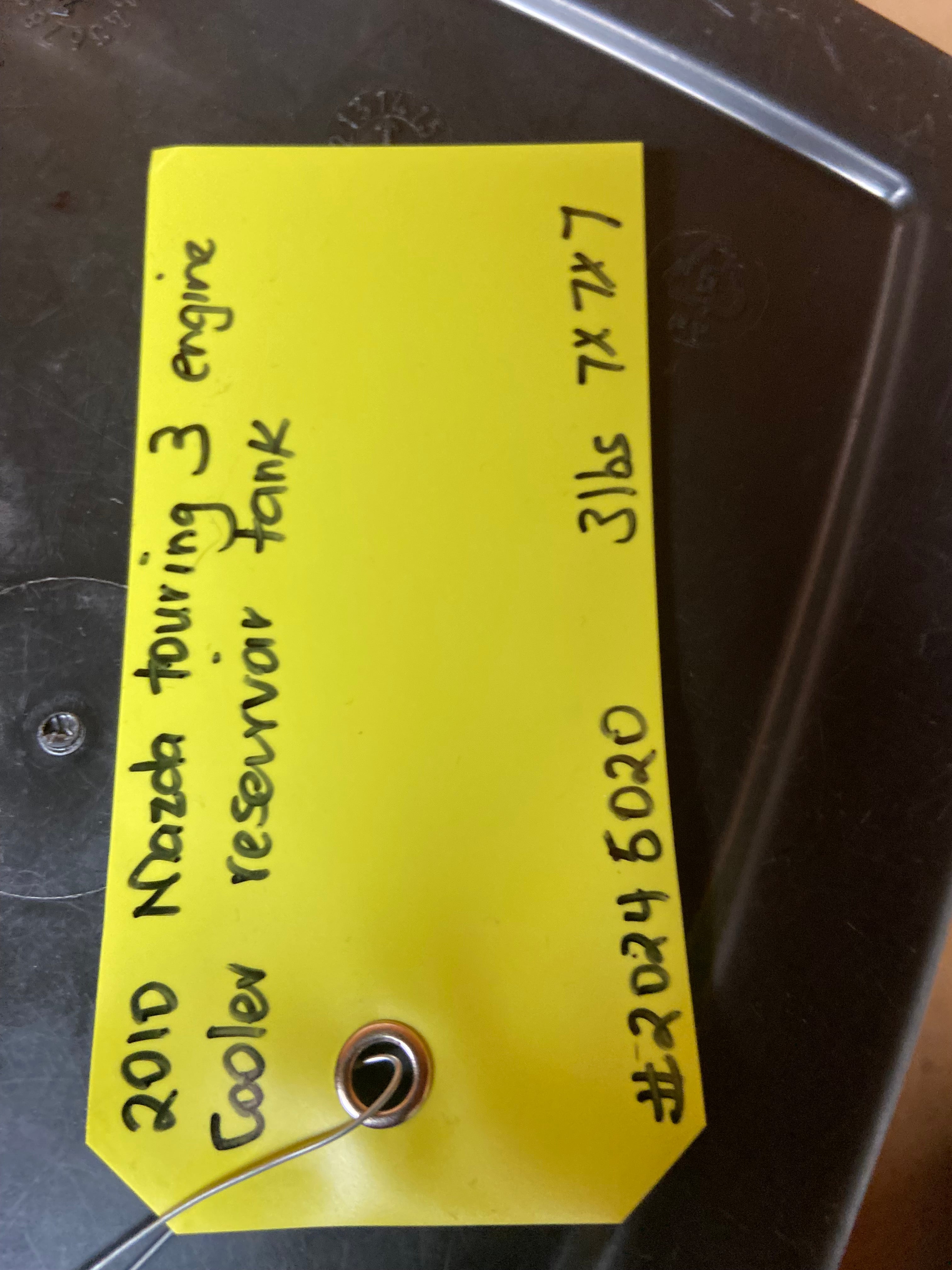 Engine coolant reservoir tank with yellow inventory label and metal filler neck