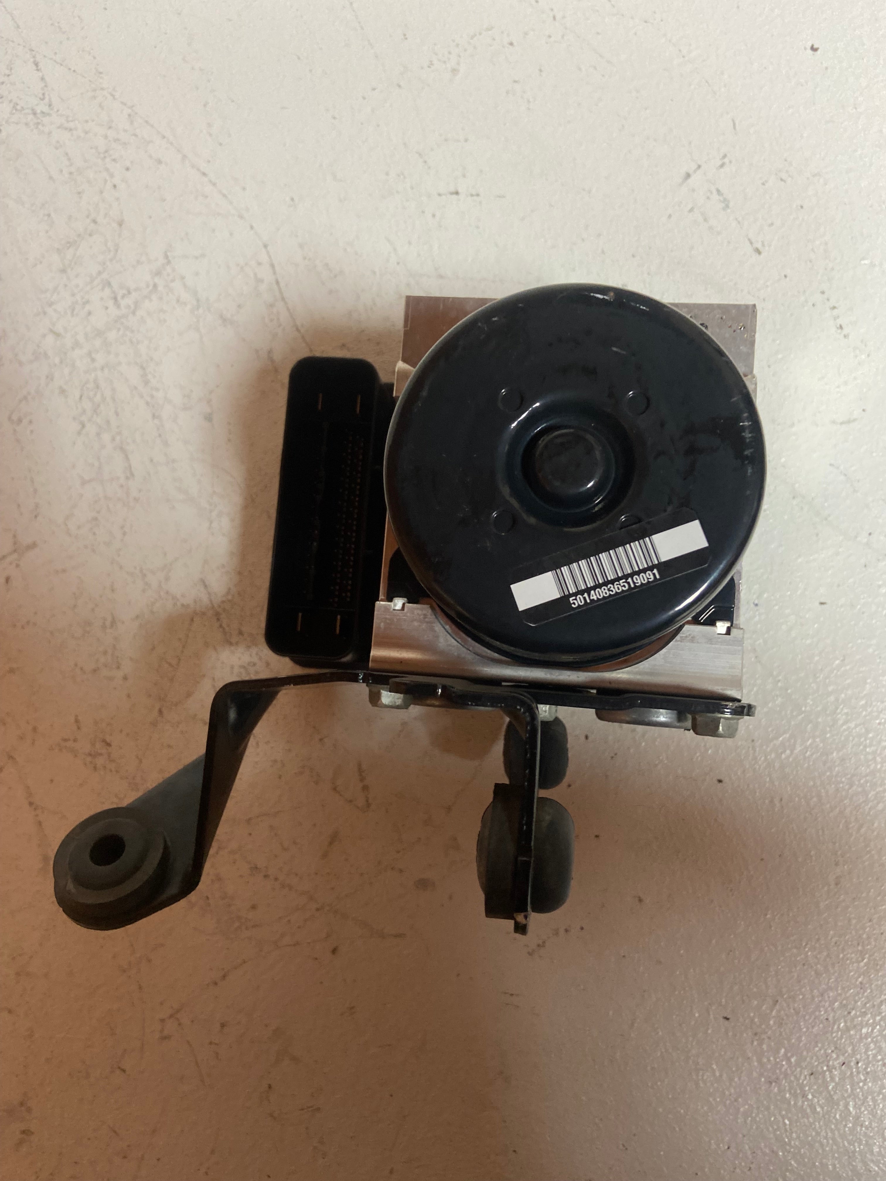 ABS pump control module with round black actuator and side mounting brackets.