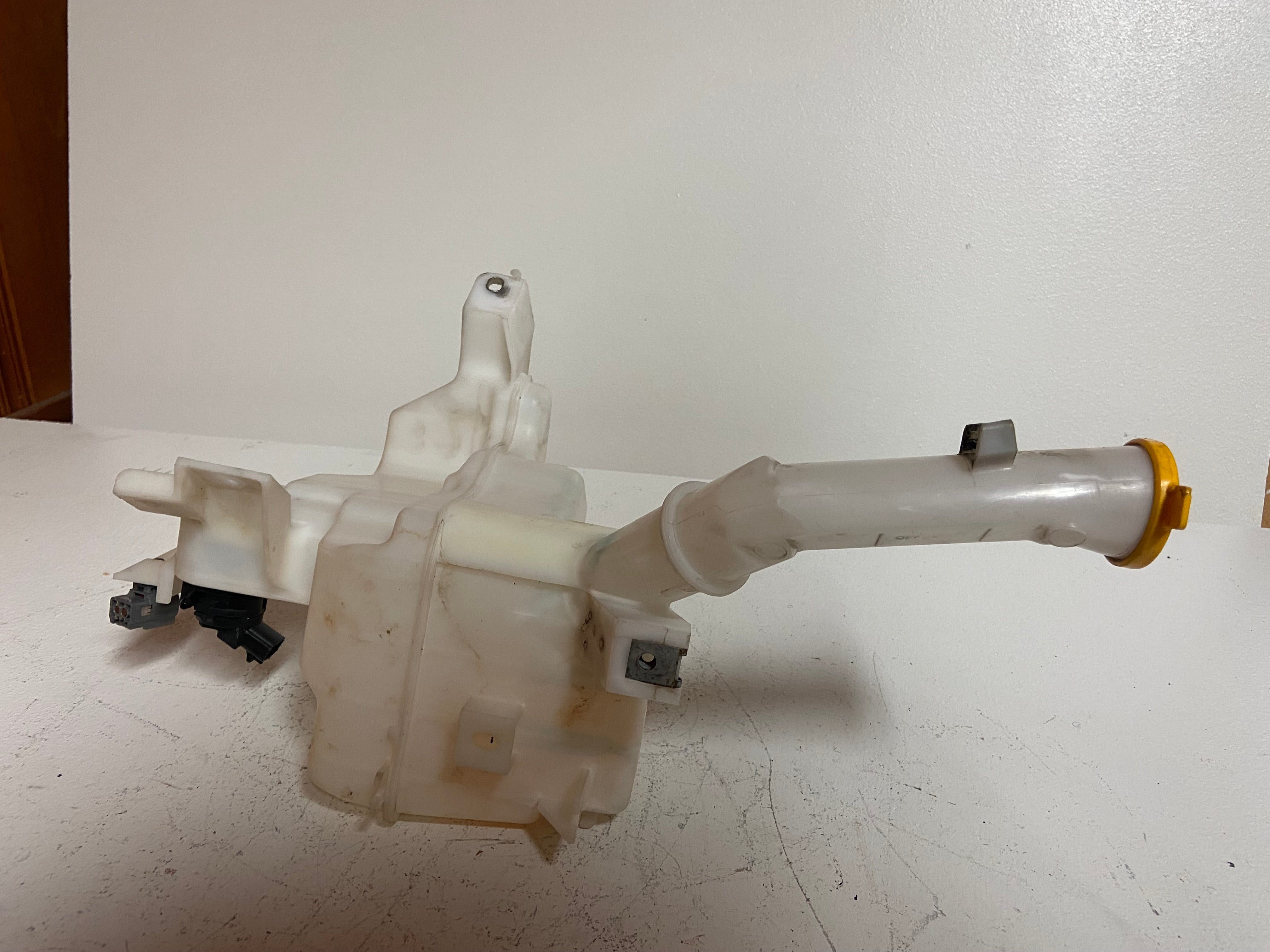 Windshield washer fluid reservoir tank with attached hoses and yellow-tipped tube