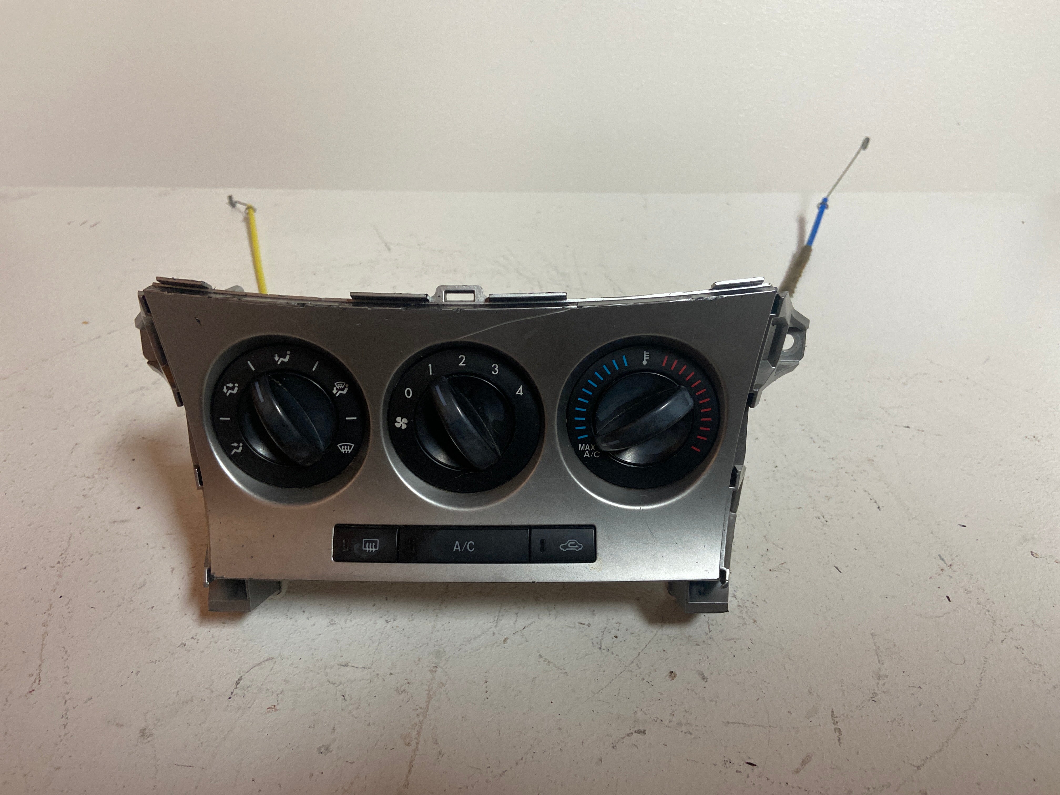 Manual climate control panel with three rotary knobs and A/C buttons; cable mount tabs