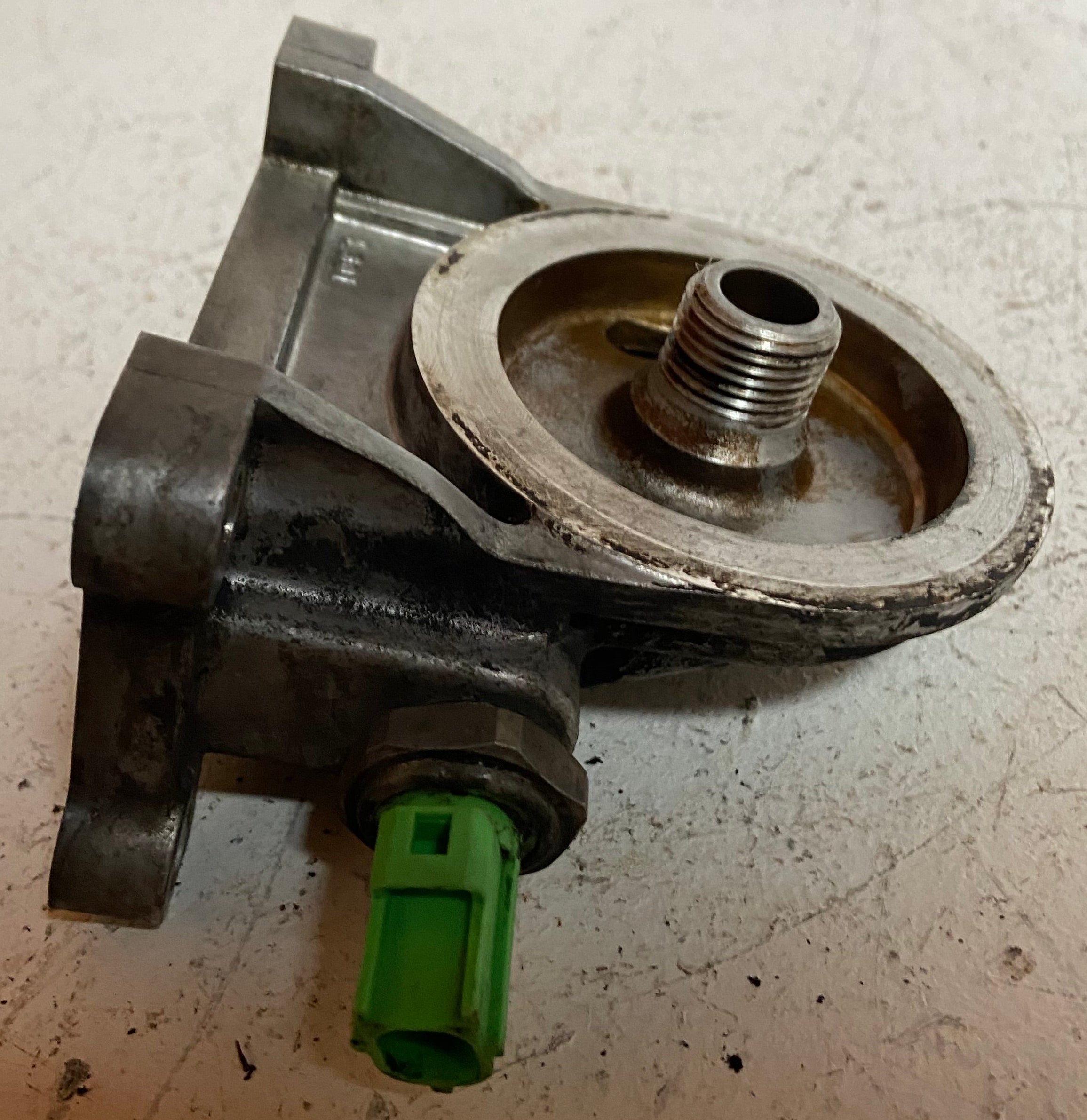 Engine oil filter adapter housing with circular opening and green electrical plug