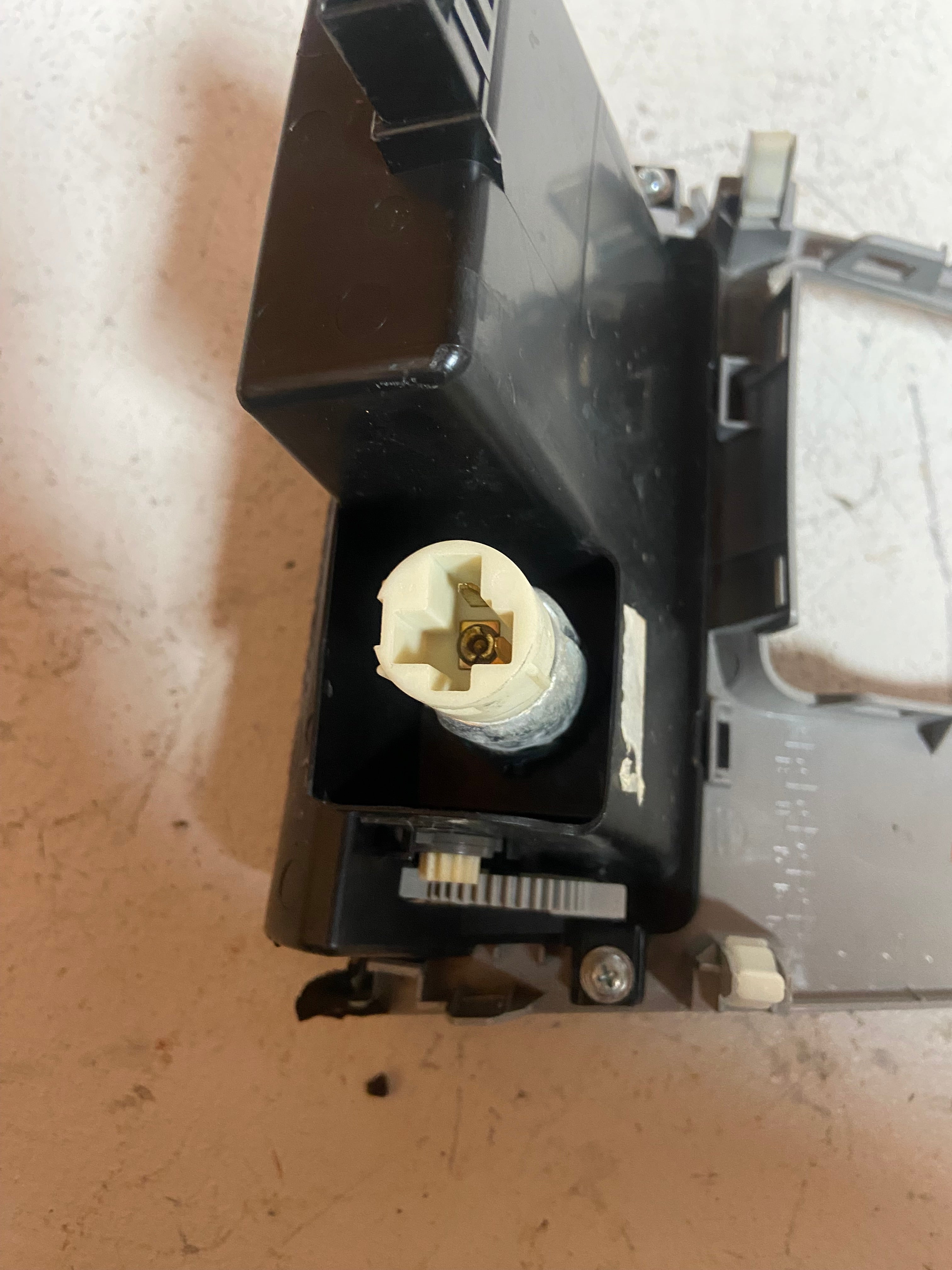 Center console shifter trim bezel with exposed mounting pegs and cream-colored connector