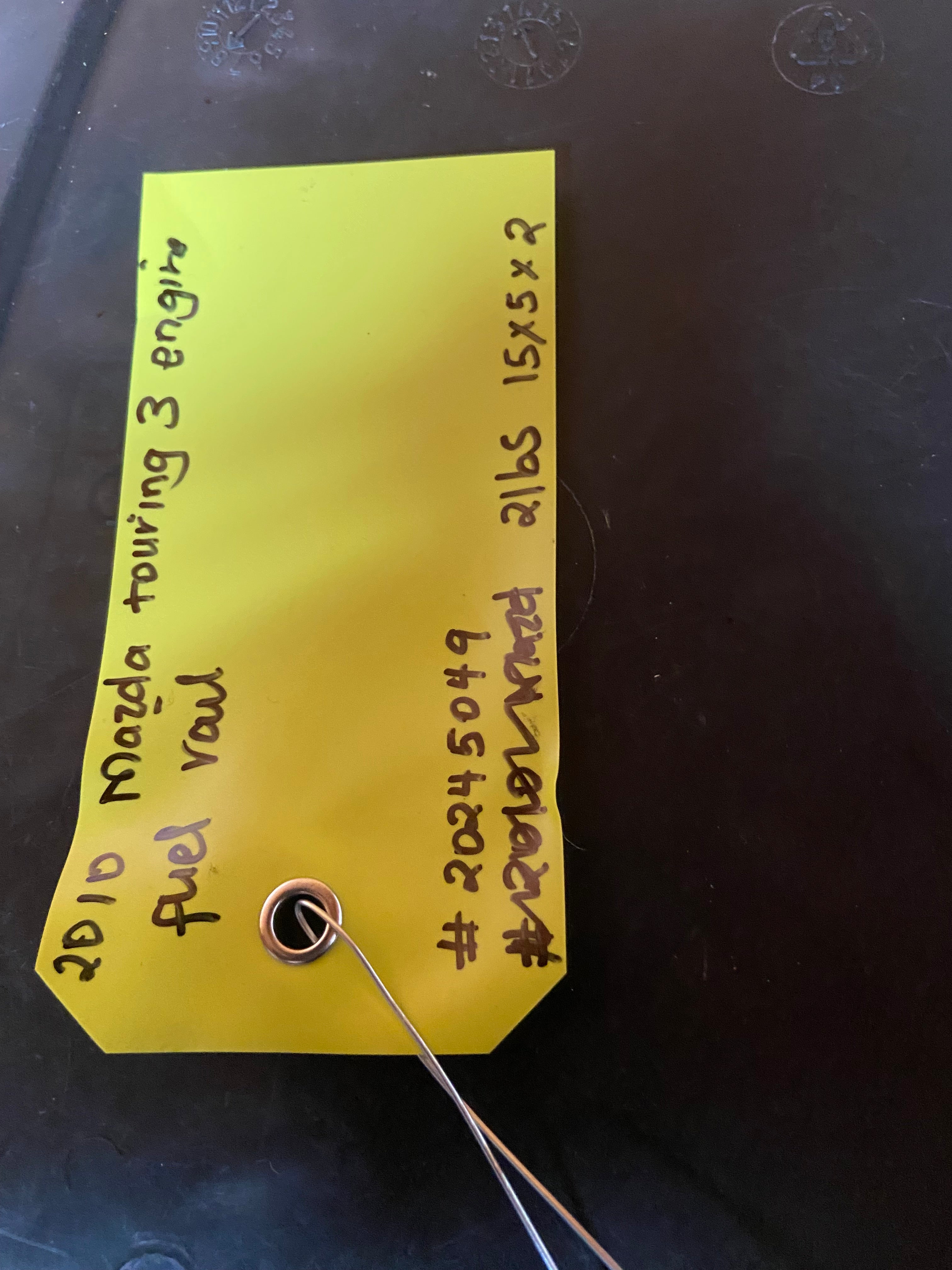 Fuel rail part with yellow inventory tag and attached metal connector pin