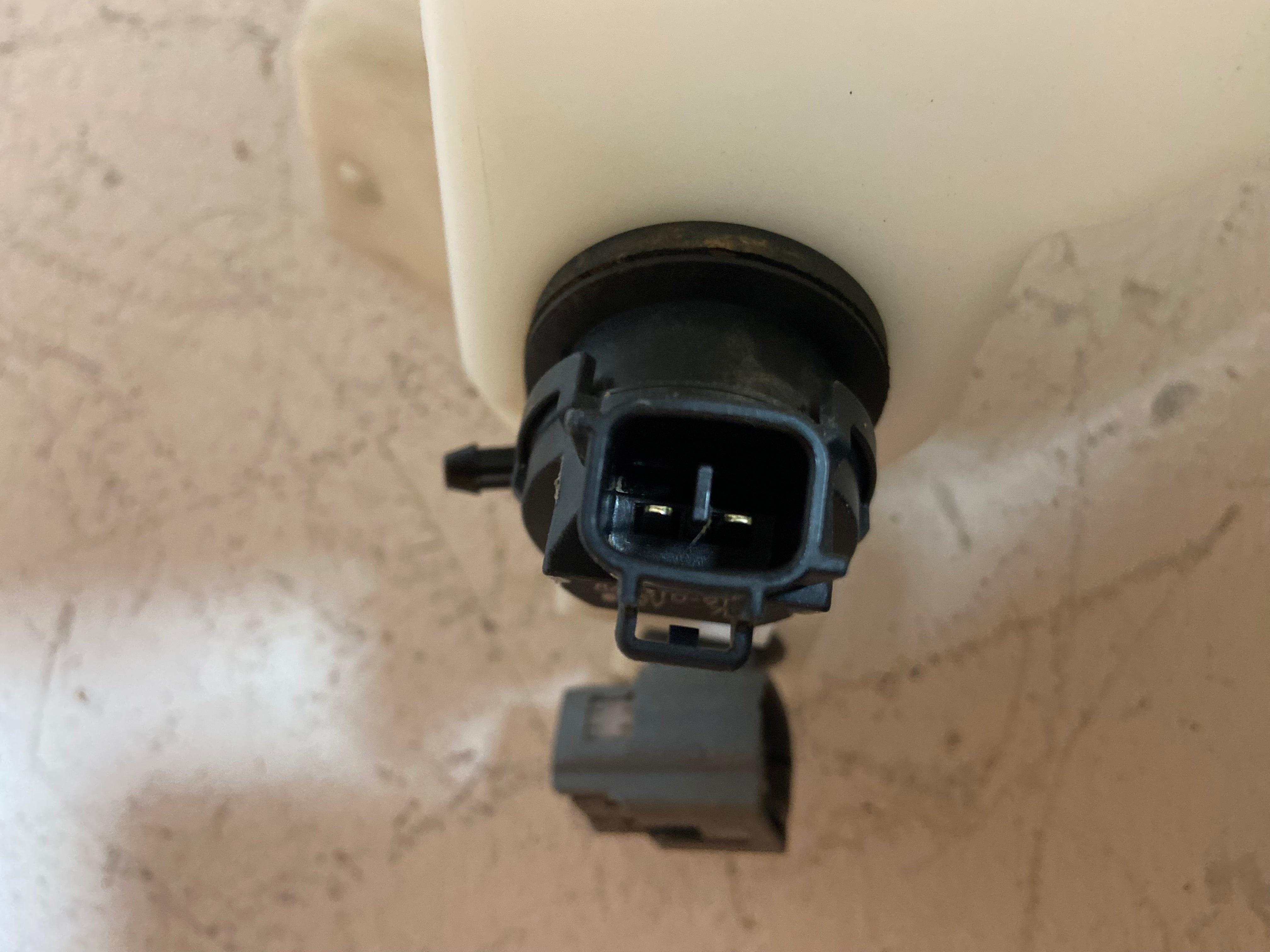 Washer fluid reservoir cap area with black round sensor housing and electrical connectors