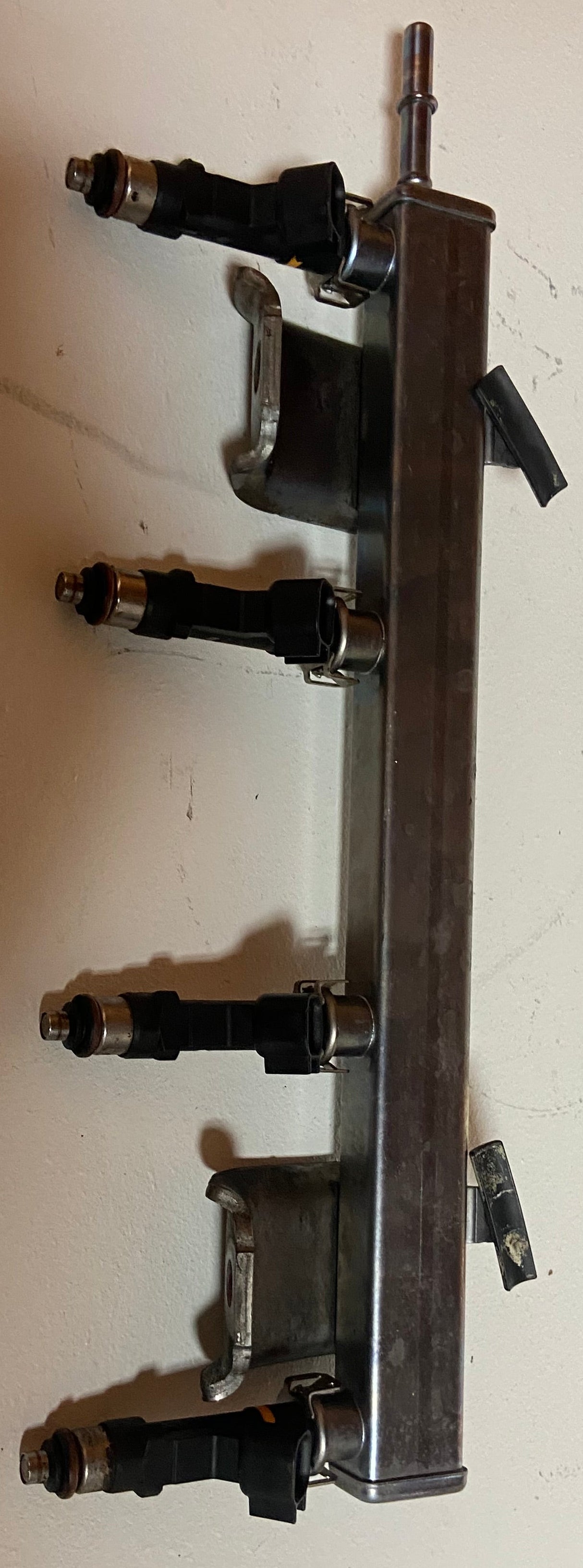 Metal engine fuel rail with four black injector connectors along the bar