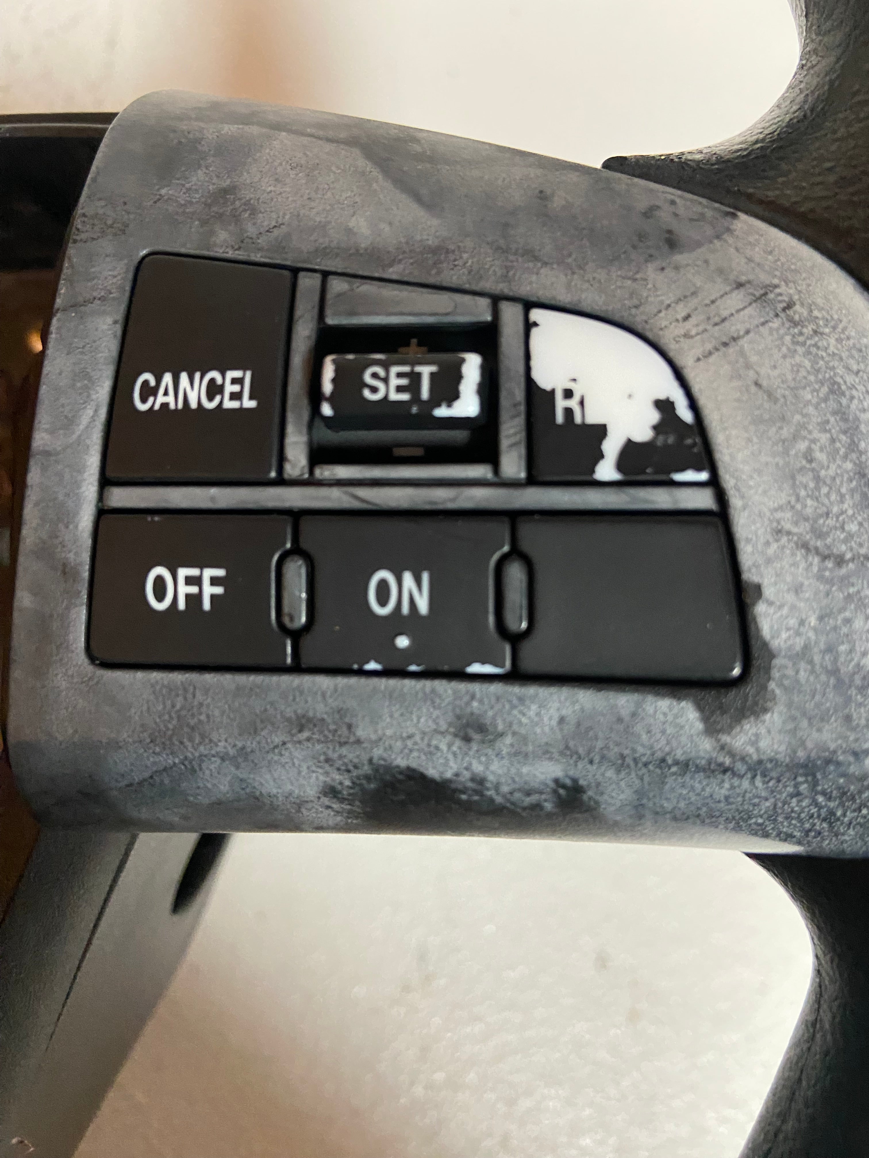 Black steering wheel control buttons: CANCEL, SET, OFF/ON, R indicator