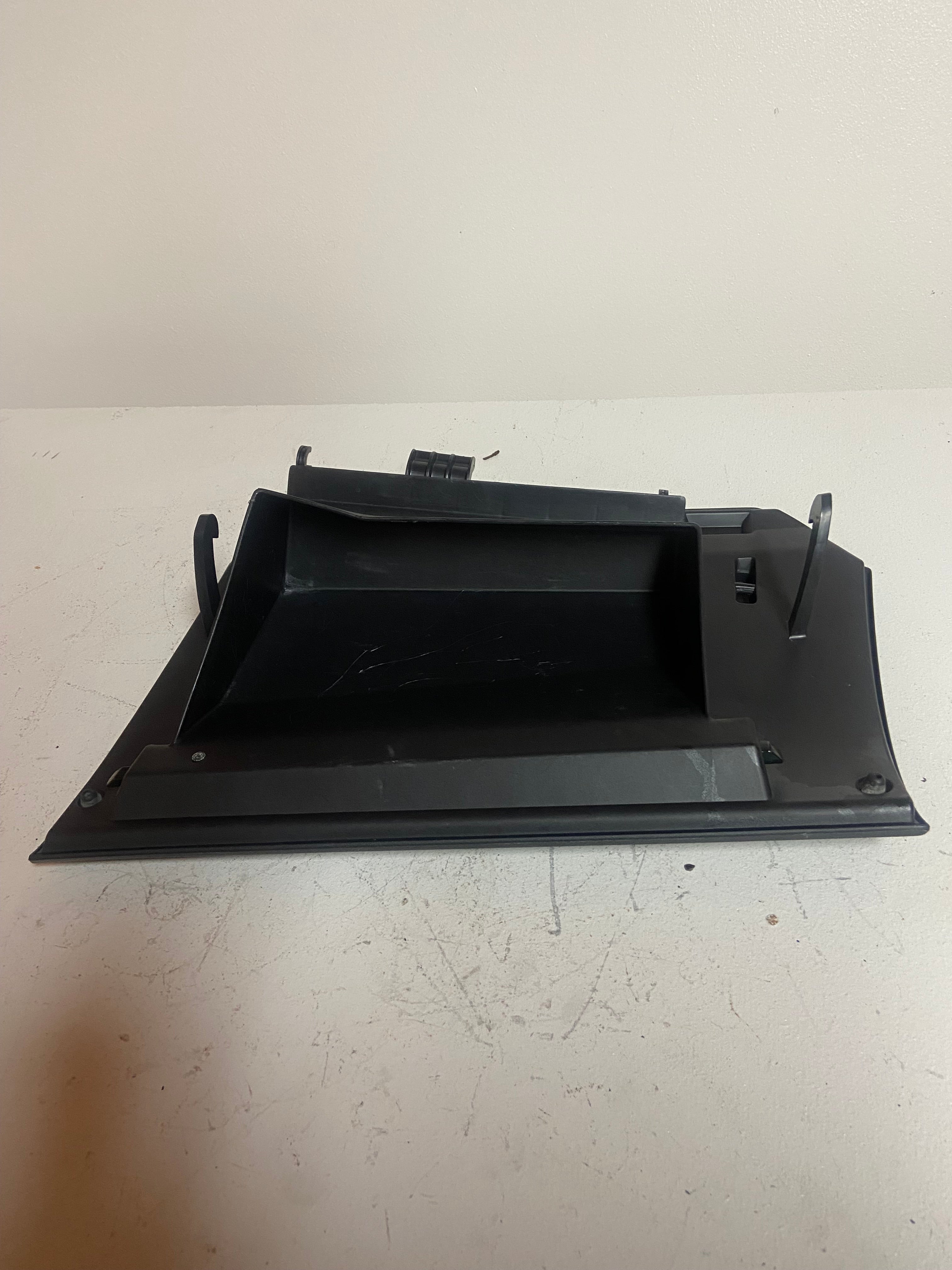 Black glove box lid base with open interior compartment, underside view