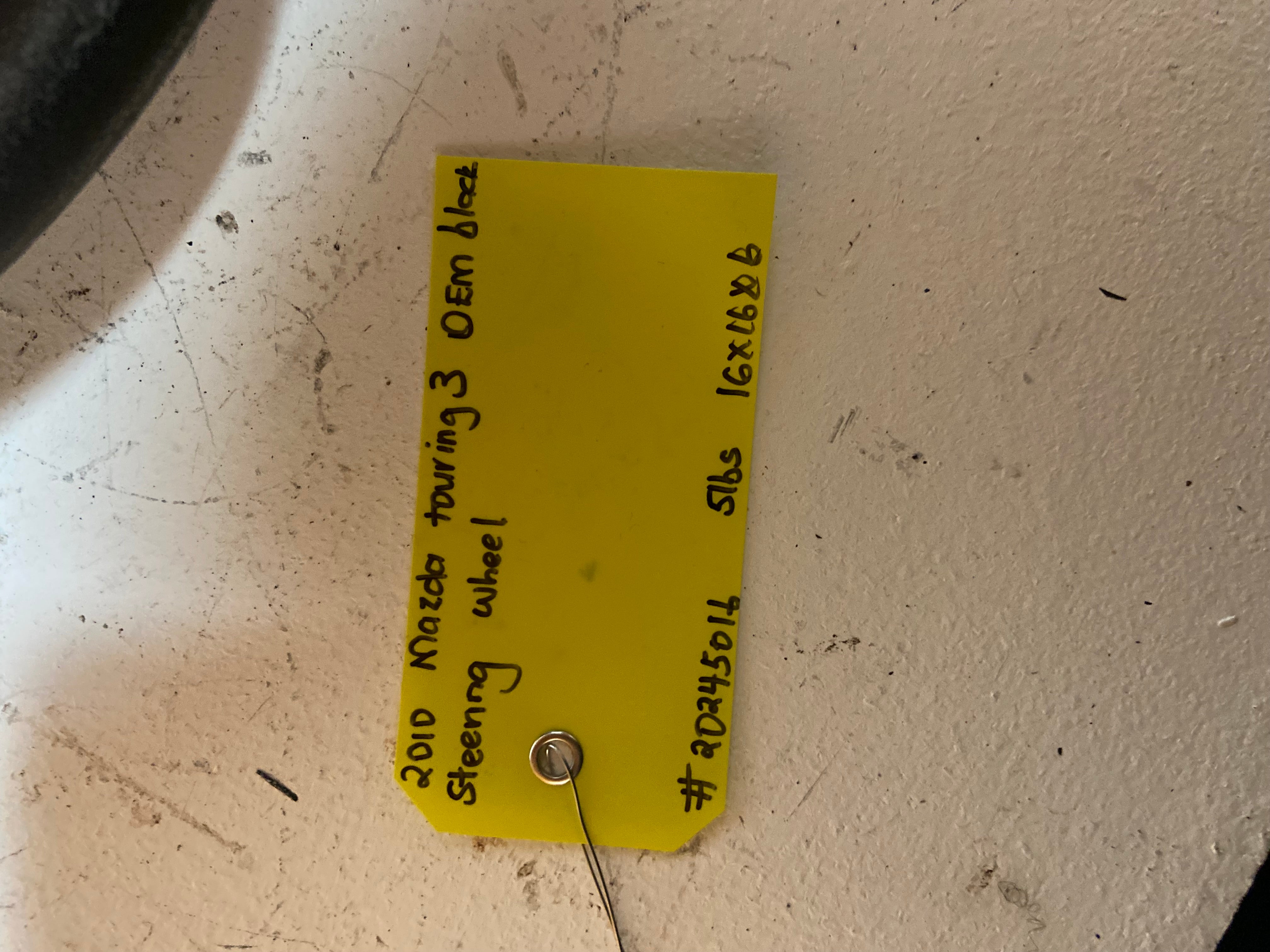 Yellow tag with handwritten parts info and key ID attached to steering wheel