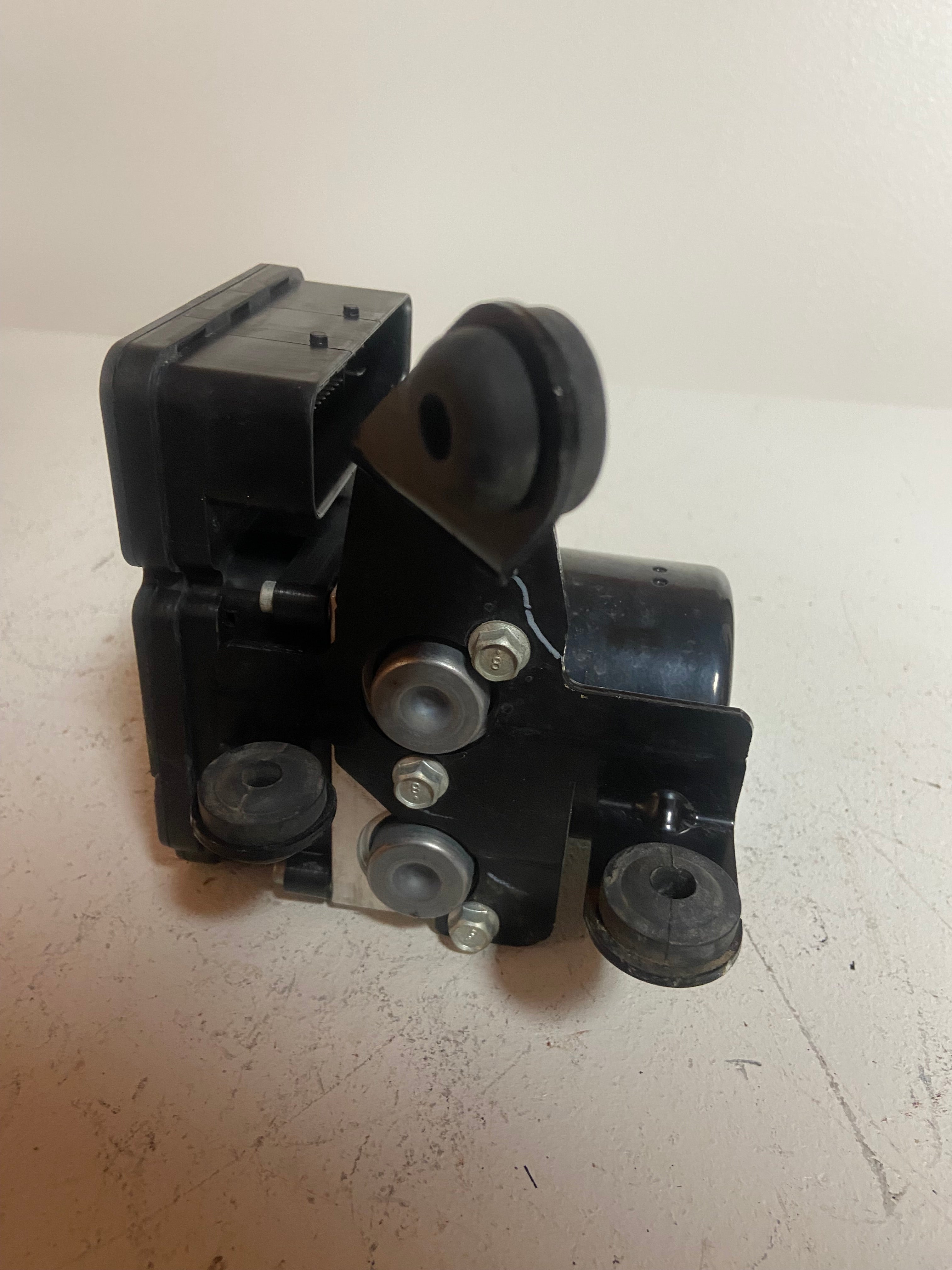 ABS pump control module with black housing and metal actuator bracket.