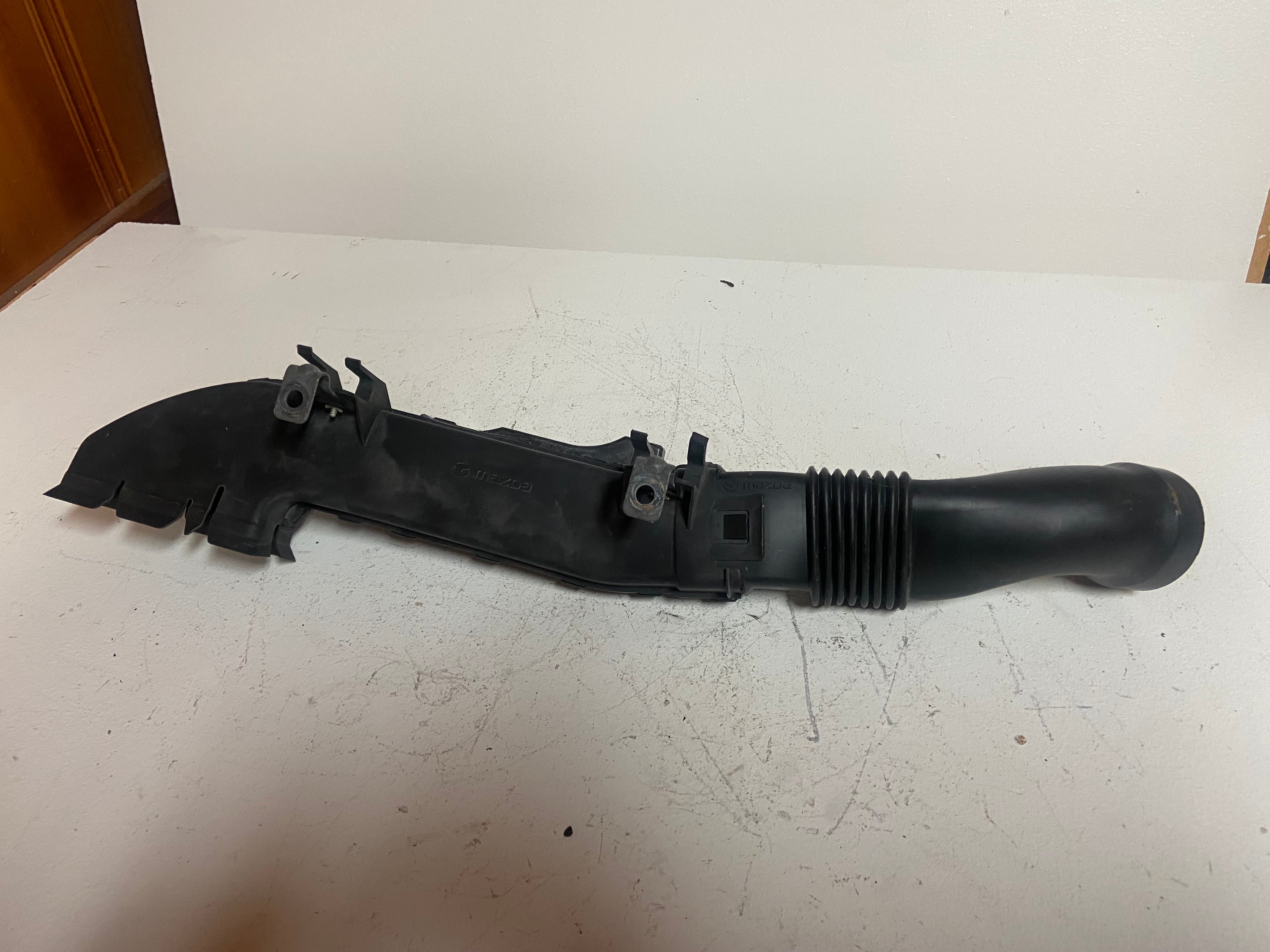 Black plastic engine air intake duct with ribbed hose section and air inlet shield