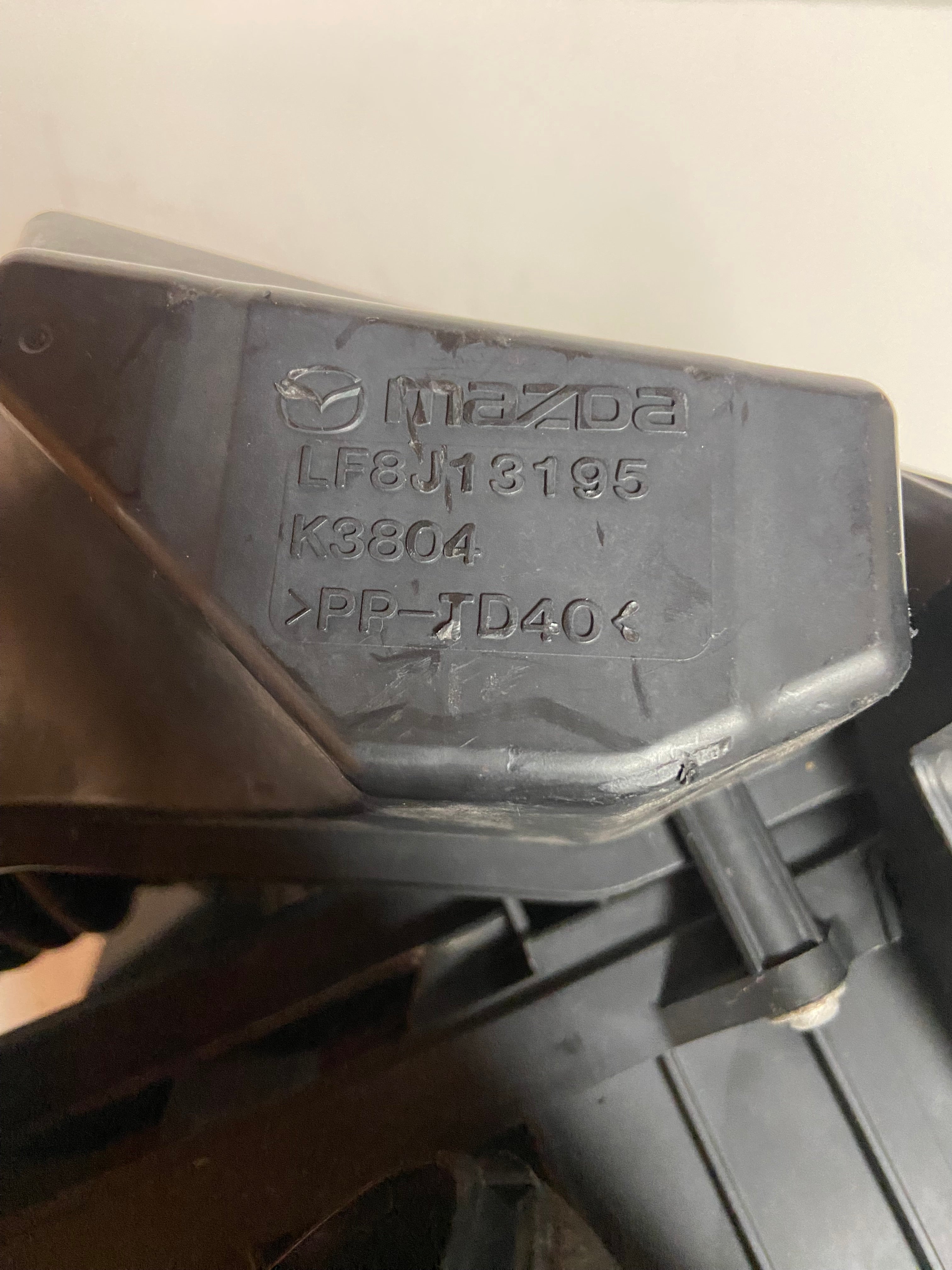 Mazda air filter housing cover with molded part numbers on black plastic