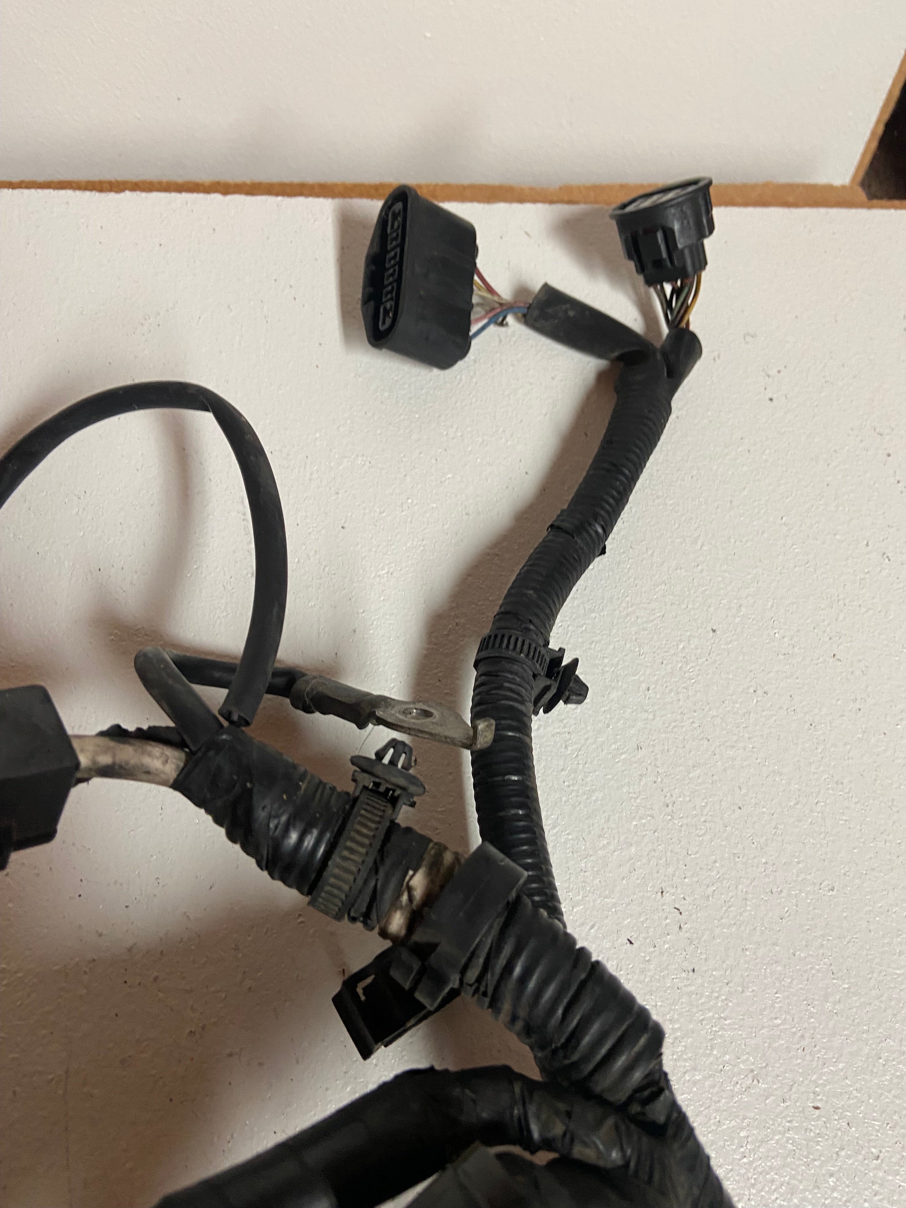 Engine wiring harness with large black connectors and wrapped black cable loom, angled.
