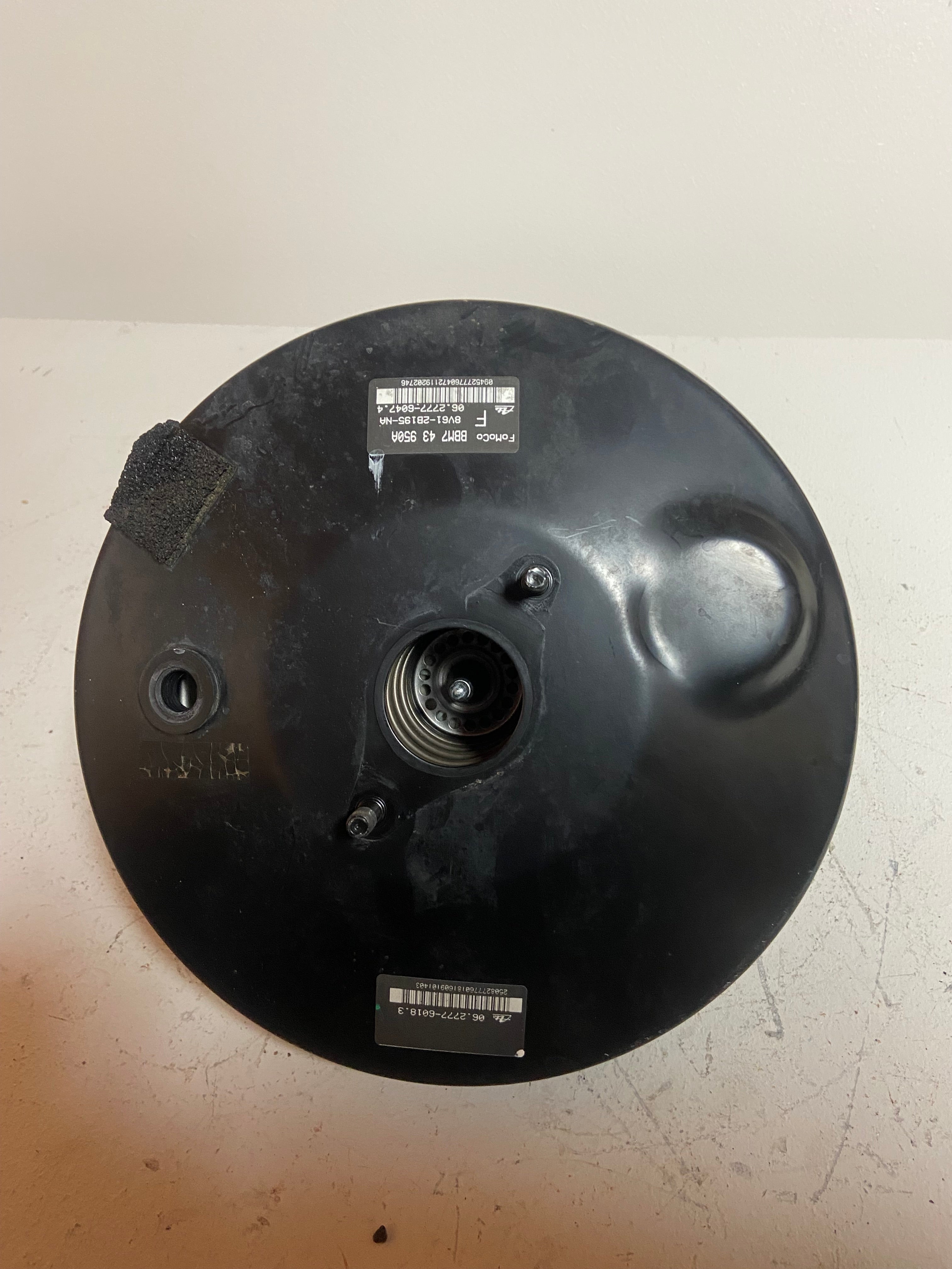 Black brake booster back view with center opening and multiple labels