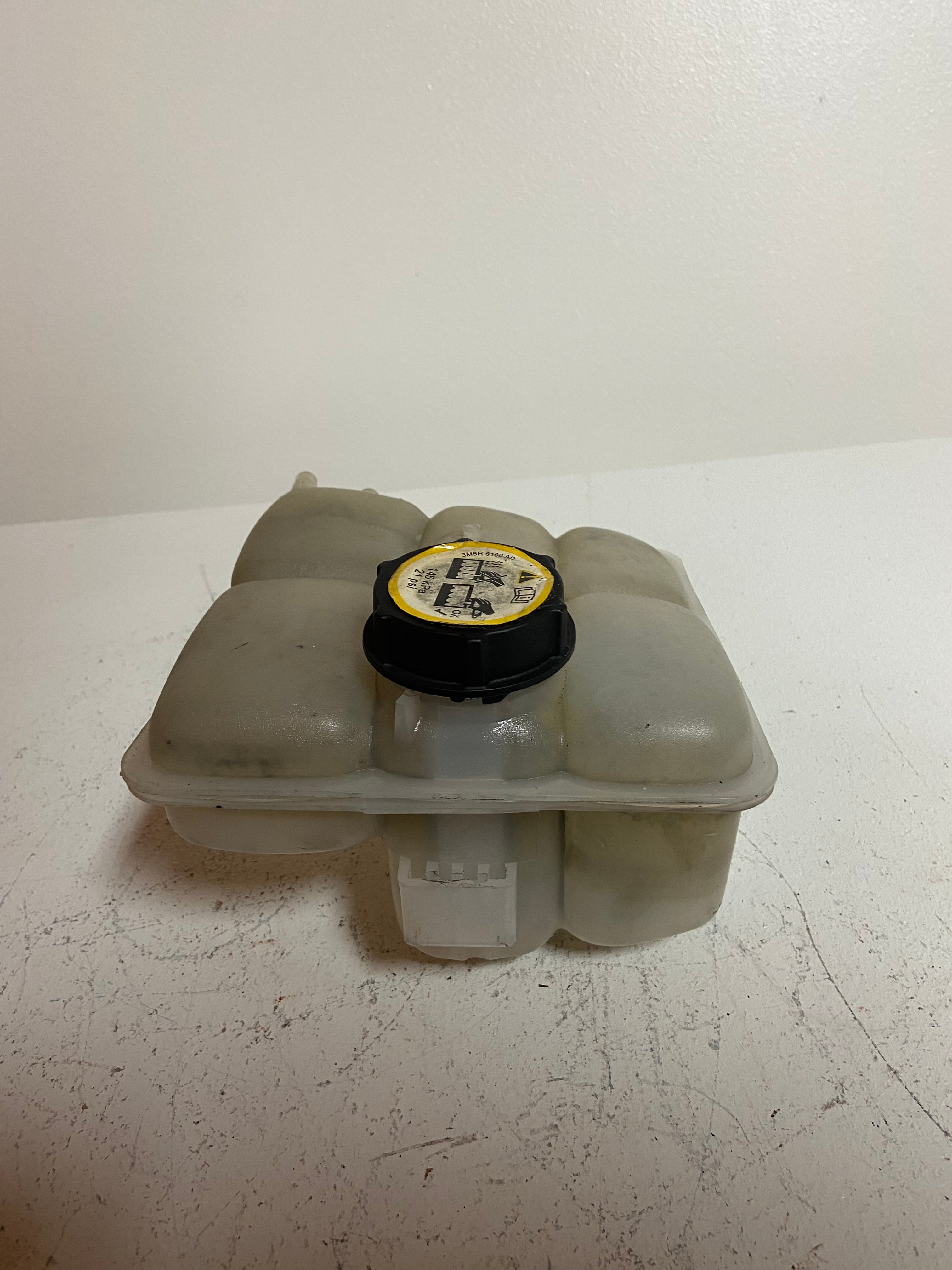 Engine coolant reservoir tank with black cap, front view of molded hose openings
