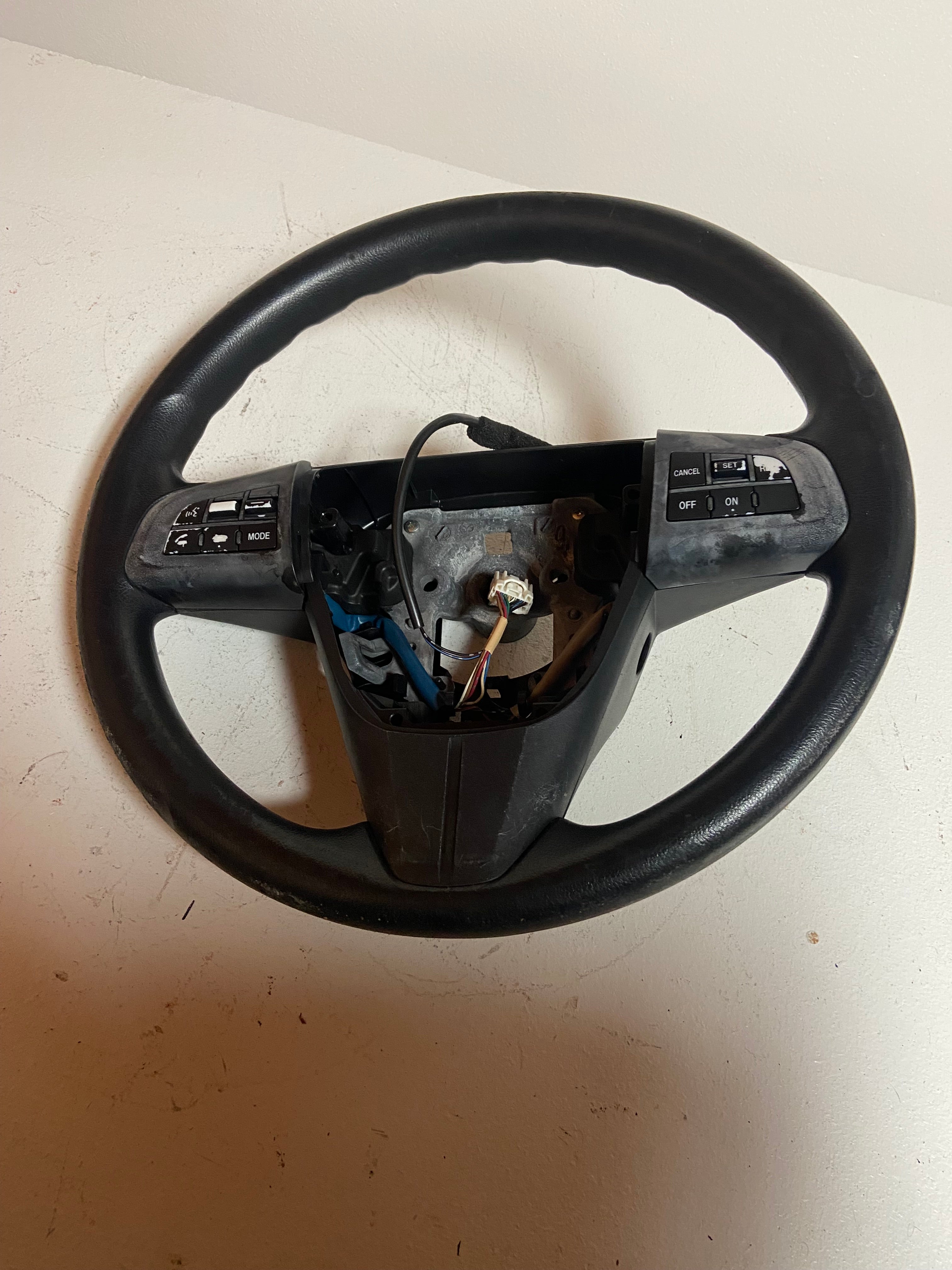 Black OEM steering wheel for 2010 Mazda 3 touring, viewed from front with controls visible