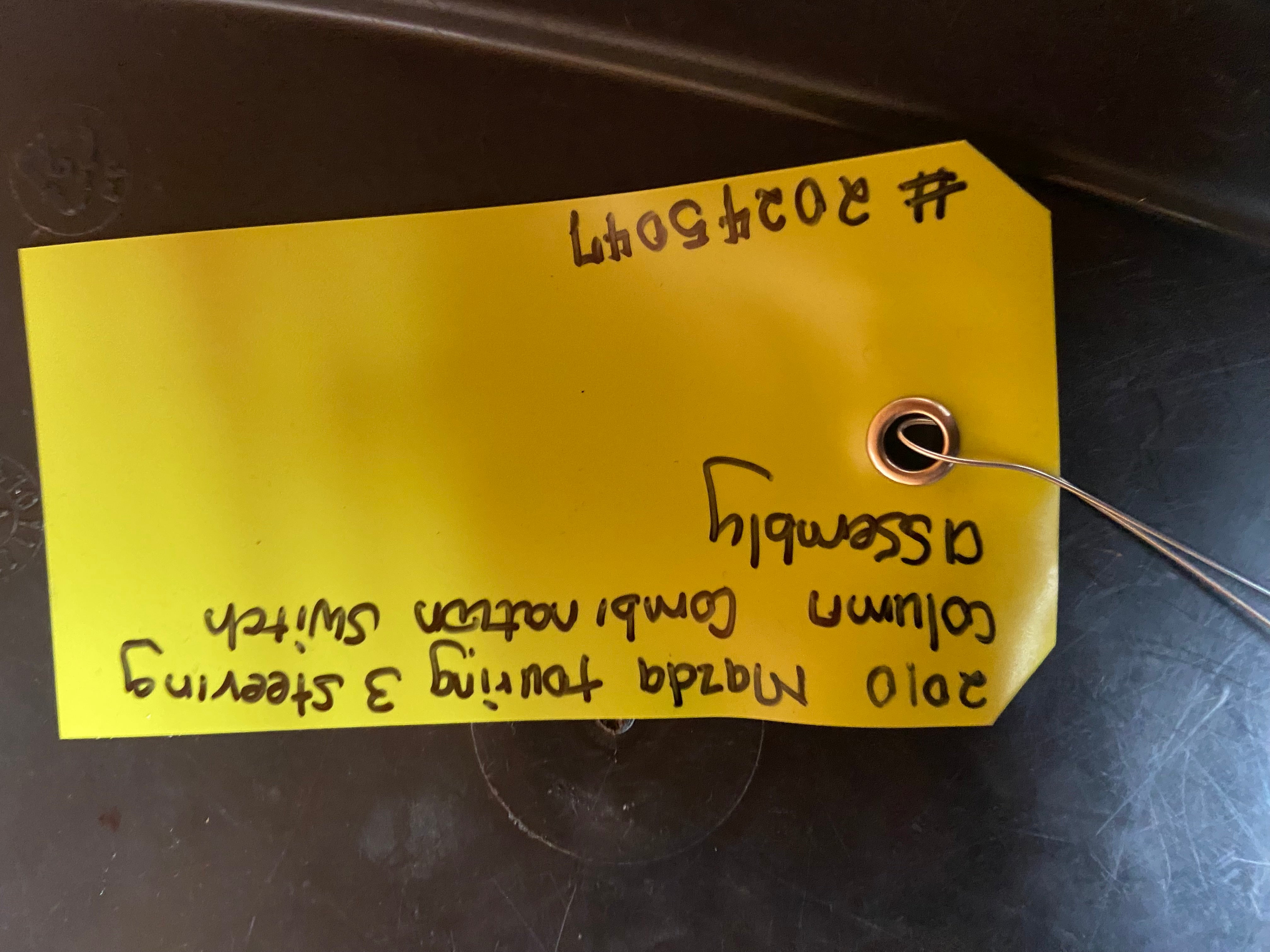 Yellow tag with handwritten notes attached to steering column switch assembly